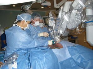 Dr. Kazuhiro Yasufuku, Director of the Interventional Thoracic Surgical Program at Toronto General Hospital, University Health Network; Dr. Tom Waddell, thoracic surgeon and Head of the Division of Thoracic Surgery and thoracic surgical fellow Dr. Mauricio Pipkin carefully attach the first of the four robotic arms on to one of the steel ports in the patient’s chest. The robotic arms are docked on to the four ports through which surgical instruments and camera are maneuvered by the surgeon sitting in a console with a monitor and hand controls several feet away from the patient.