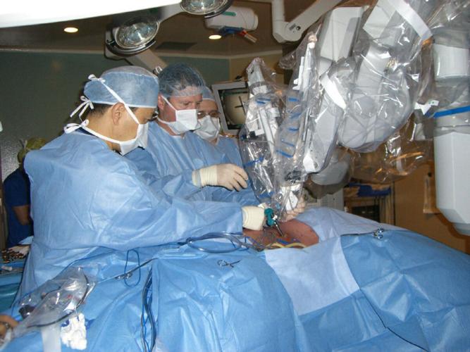 Dr. Kazuhiro Yasufuku, Director of the Interventional Thoracic Surgical Program at Toronto General Hospital, University Health Network; Dr. Tom Waddell, thoracic surgeon and Head of the Division of Thoracic Surgery and thoracic surgical fellow Dr. Mauricio Pipkin carefully attach the first of the four robotic arms on to one of the steel ports in the patient’s chest. The robotic arms are docked on to the four ports through which surgical instruments and camera are maneuvered by the surgeon sitting in a console with a monitor and hand controls several feet away from the patient.